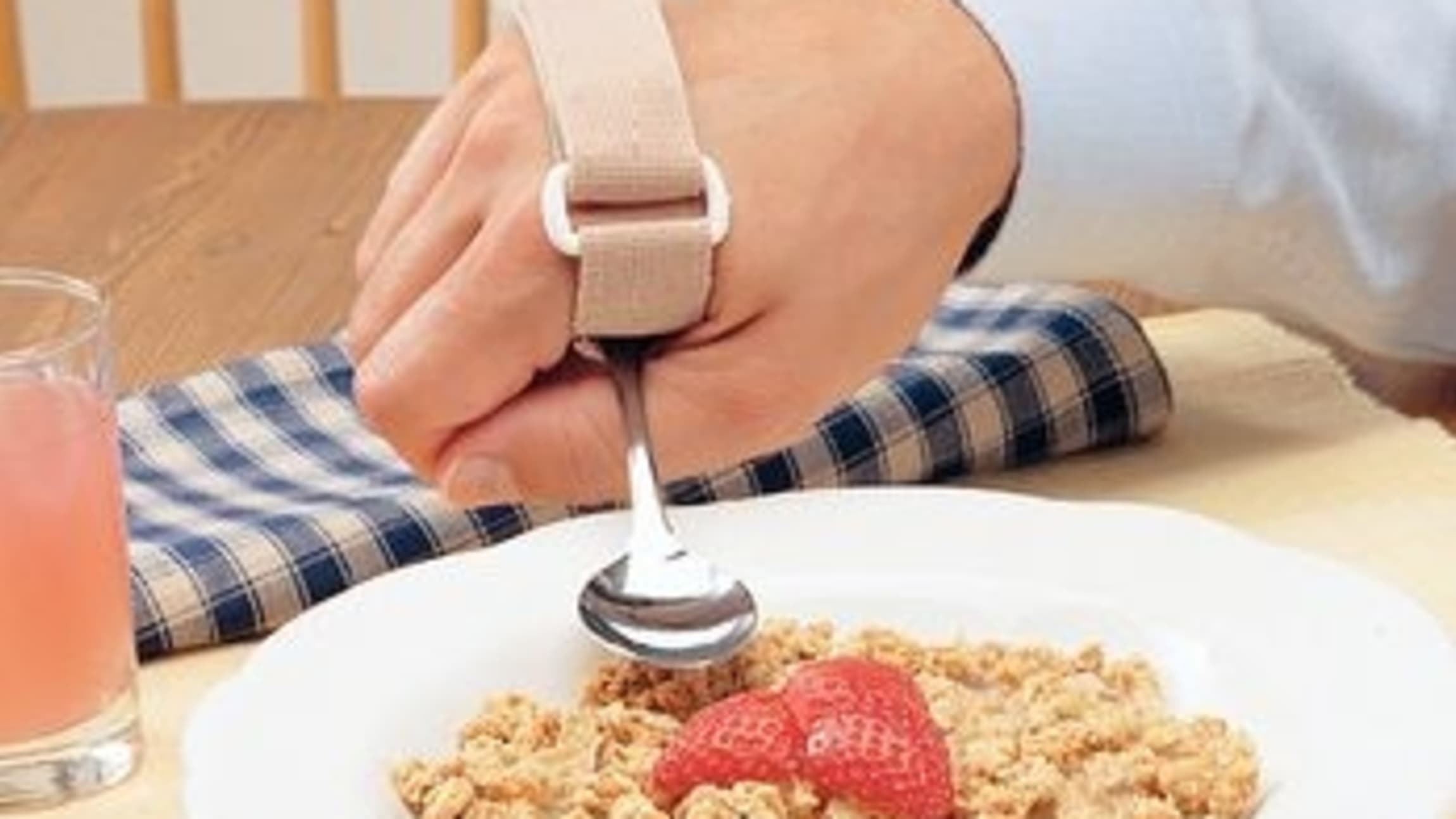 Someone using a universal cuff to eat a bowl of cereal.