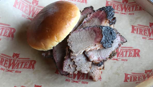 Sliced brisket and a bun on branded 'Firewater BBQ Brew' paper.