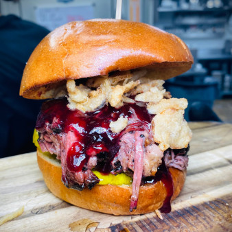 Close-up of a brisket sandwich with sauce, onions, and pickles on a bun.