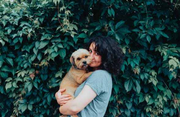 Woman holding puppy in front of green leaves