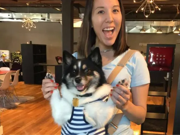 a woman with a dog satchel hugging her dog, they are both smiling