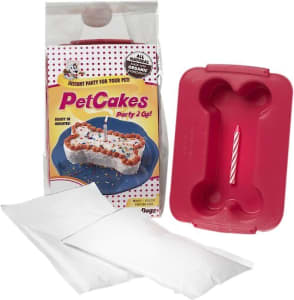 A box of microwavable birthday cake mix for dogs next to a red bone-shaped cake pan