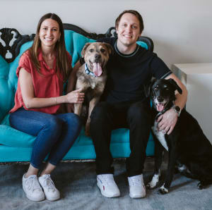 Sugar Snap sits on a blue couch between his adopters, Dr. Ritchie and Dr. Yesesky, with dog brother Fitz.