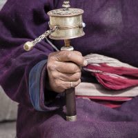 Old Tibetan woman holding buddhist prayer wheel.