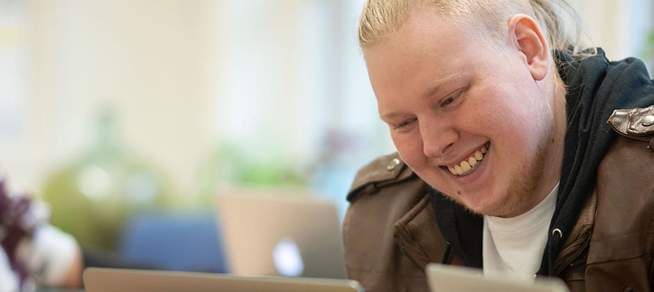 Löftadalens folkhögskola Ung person skrattar och skriver på sin dator.