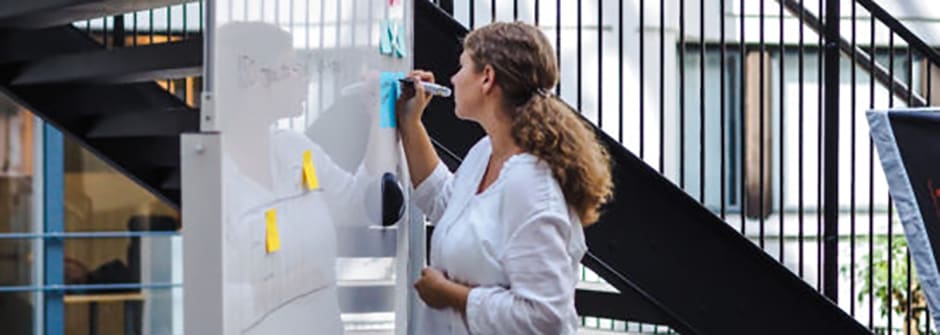 Asiantuntijatyön Lean-työkaluja Kuvassa nainen ja whiteboard, jossa post it -lappuja