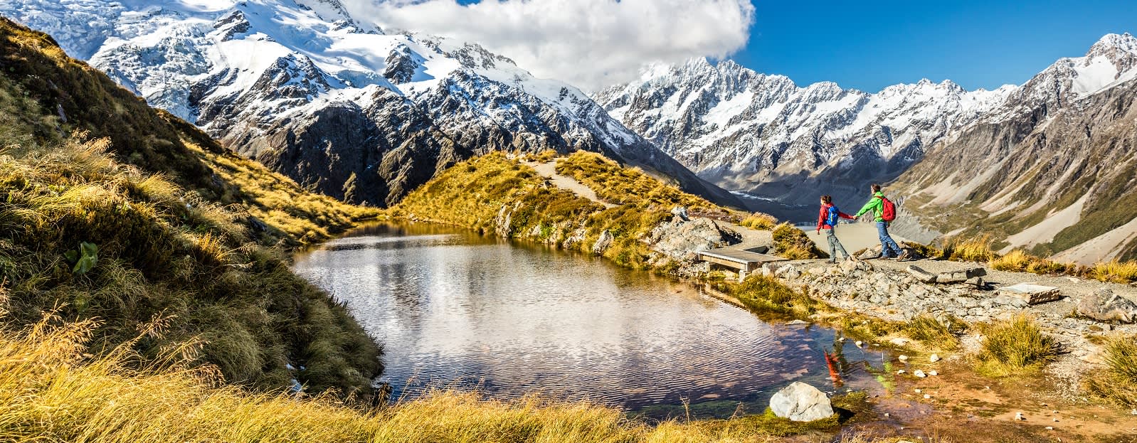 Hiking travel nature hikers in New Zealand. Couple people walking on Sealy Tarns hike trail route with Mount Cook landscape, famous tourist attraction - New Zealand travel