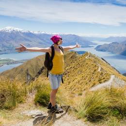 Junge Frau mit ausgestreckten Armen auf einem Berg in Neuseeland