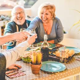 Gruppe älterer Menschen prostet sich an einem gedeckten Tisch ausgelassen mit Weingläsern zu