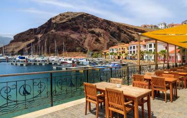 Chairs and tables of local restaurant in harbour with boats and yachts and colorful houses, Madeira island, Portugal