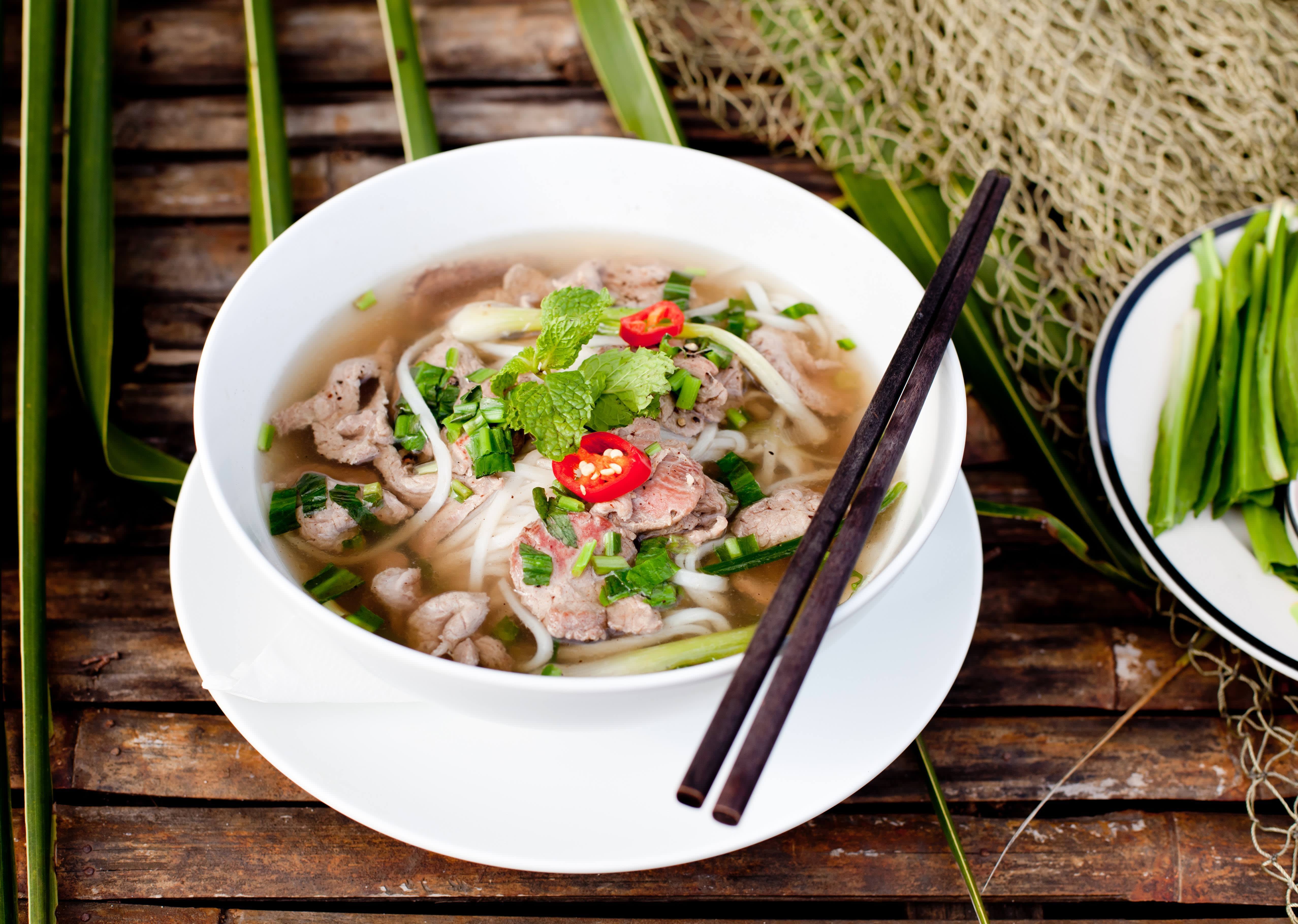 Eine vietnamesische Pho mit Koriander, Rindfleisch und Nudeln und Stäbchen über der Schüssel in Vietnam