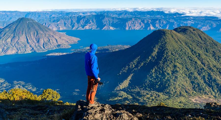 Guatemala travel guide - Enchanting TravelHiker with panorama view of Lake Atitlan and volcano San Pedro and Toliman early in the morning from peak of volcano Atitlan, Guatemala. Hiking and climbing on Vulcano Atitlan