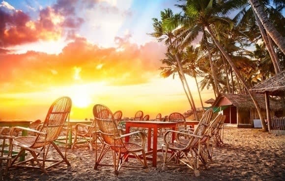 Tische und Stühle auf Sandstrand bei Sonnenuntergang in Südindien