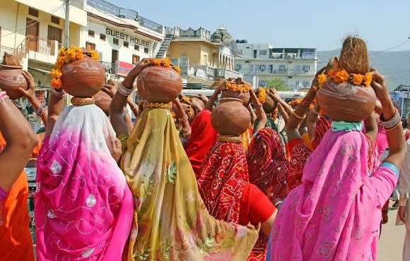 Frauen in bunter traditioneller Kleidung tragen Schüsseln auf ihren Köpfen, Indien