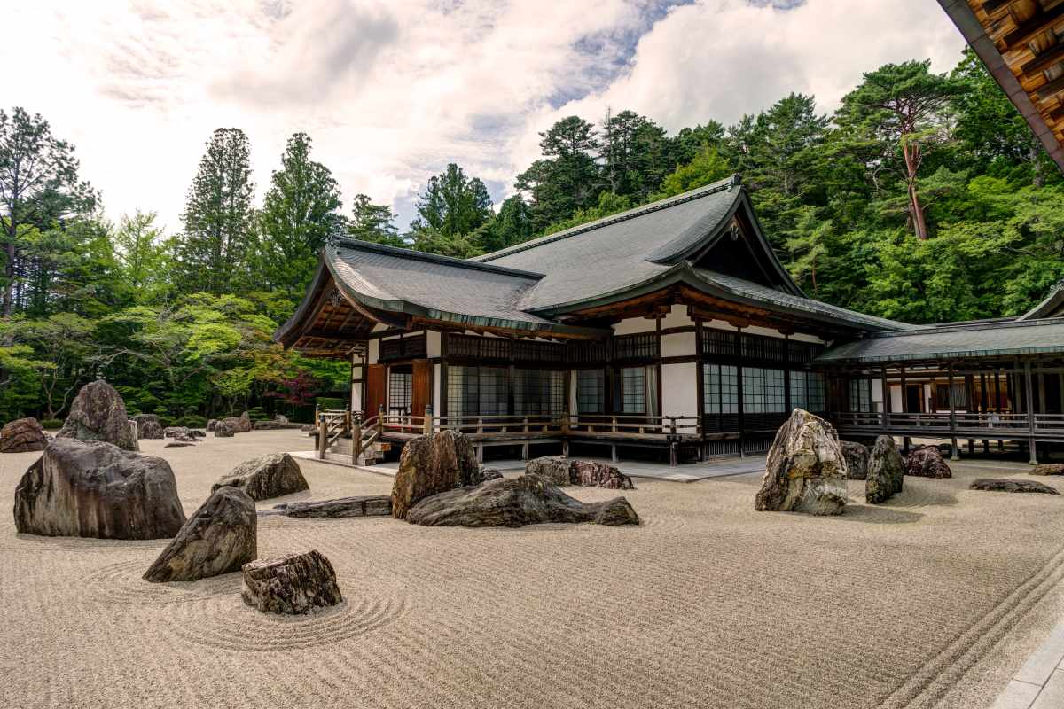 A raked gravel Zen rock garden fronting a traditional temple building, framed by forested hills.