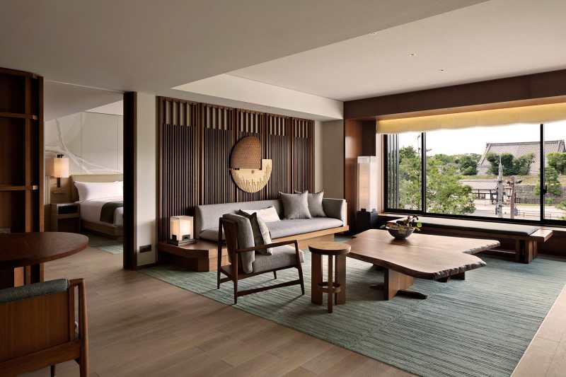 A serene contemporary hotel suite with low lounge seating and a wide window opening onto greenery.
