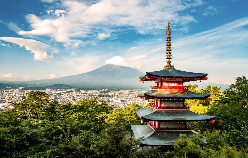 A vermilion five-storied pagoda above a town, with Mount Fuji rising in the distance.