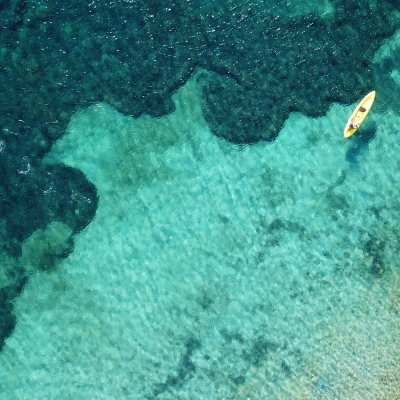 Aerial drone bird's eye view of kayaks cruising in tropical rocky seascape with turquoise and sapphire clear waters