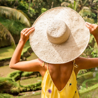Is Indonesia safe? Beautiful young lady in shine through dress touch straw hat. Girl walk at typical Asian hillside with rice farming, mountain shape green cascade rice field terraces paddies. Ubud, Bali, Indonesia