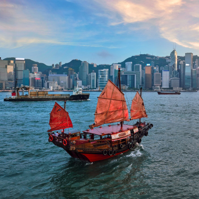Abendstimmung im Victoria Harbour in Hongkong mit traditionellem Segelboot im Vordergrund