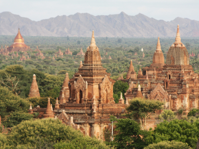 Temples and Pagodas in a forest in Bagan Myanmar with a backdrop of mountains