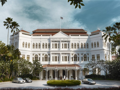 a large white building with trees in the background with Raffles Hotel in the background