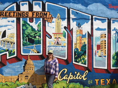 Woman standing in front of a poster saying greetings from Austin, Capitol of Texas