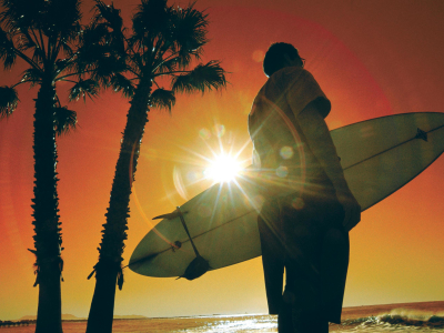 a man standing next to a palm tree in front of a sunset