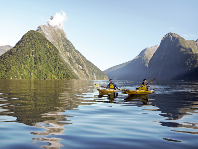 a small boat in a body of water with Milford Sound in the background