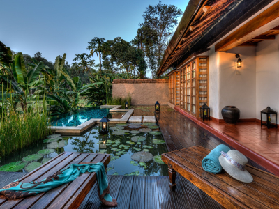 Luxury resort villa terrace with lily pond, wooden sun loungers, lanterns, and lush tropical greenery at Evolve Back, Coorg.