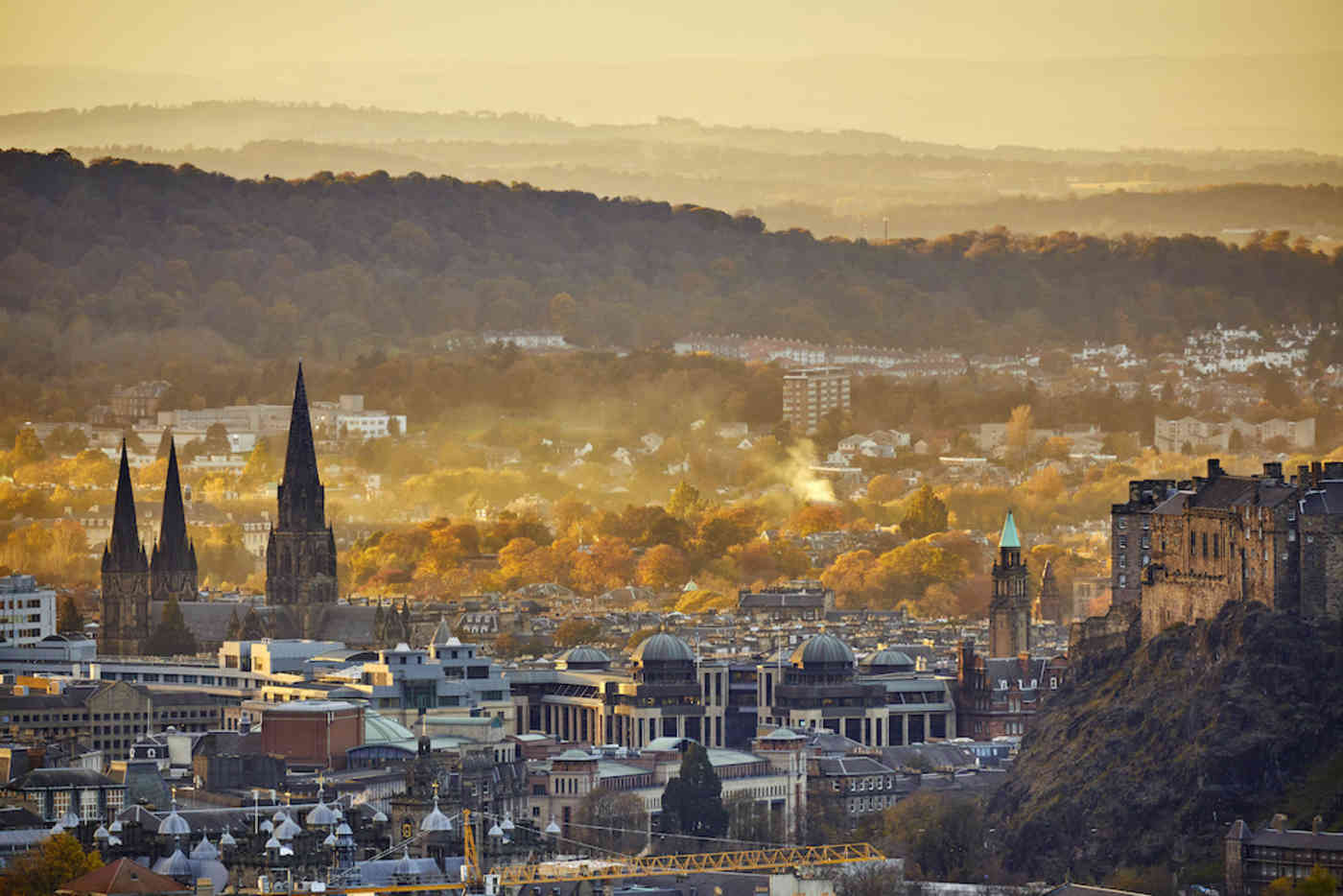 Edinburgh cityscape and mountains on skyline with St Mary's Cathedral steeples and Autumn trees