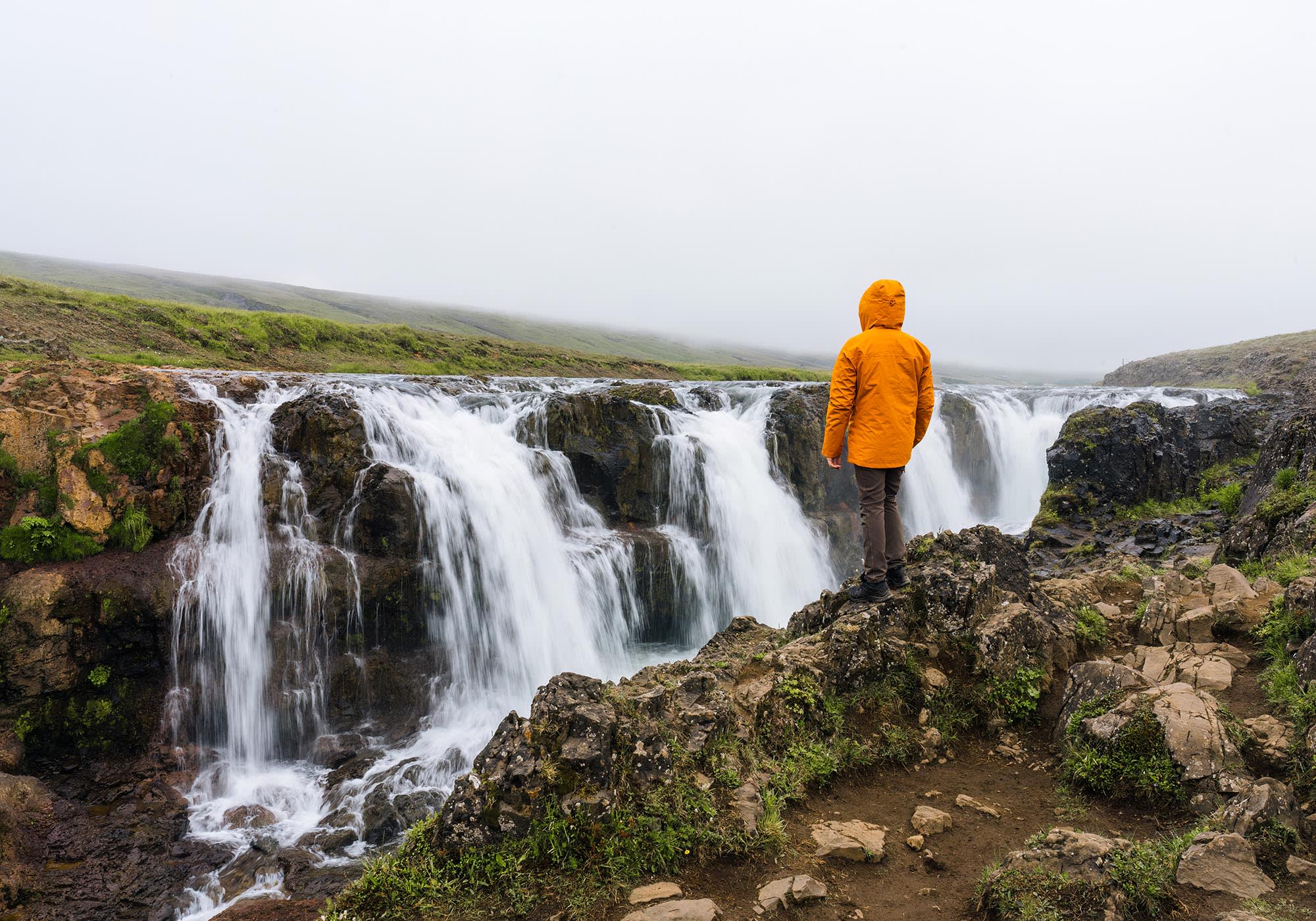 Male tourist standing and looking at Kolugljufur Canyon rapids f