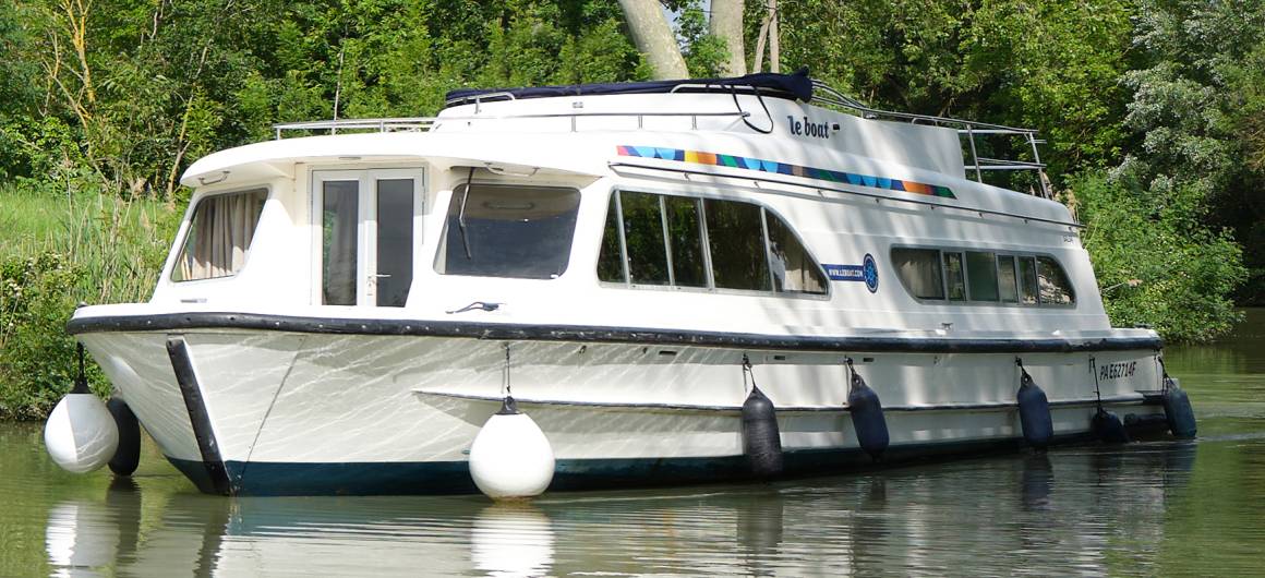 Front view of the Dancer 4 gliding down a tree-lined waterway under a bright sky.