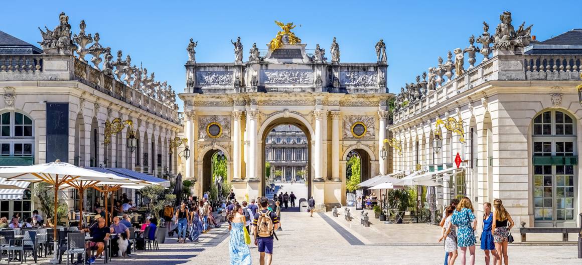 Promeneurs appréciant les cafés sur la place Stanislas, encadrée par des grilles dorées et une architecture classique.