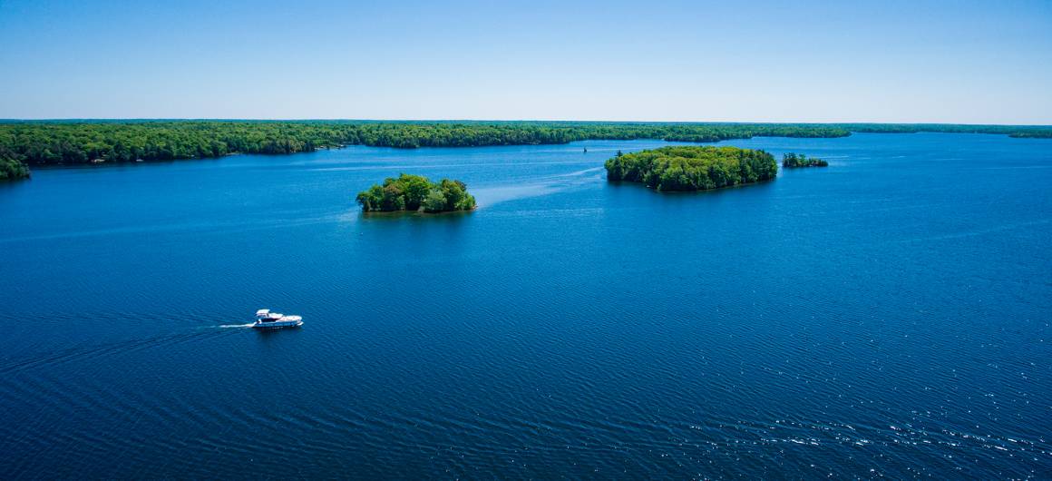 A Horizon boat cruises near small forested islands on the Rideau Canal, the deep blue water stretching toward the horizon.