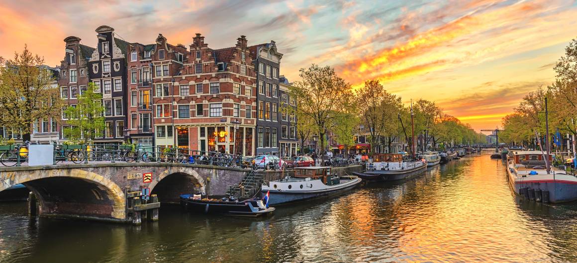 Sunset over an Amsterdam canal with historic buildings and houseboats along the water.