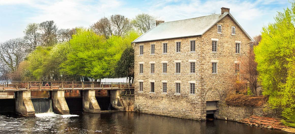 A historic stone mill stands by the locks along the Rideau Canal, surrounded by spring foliage in Ontario.