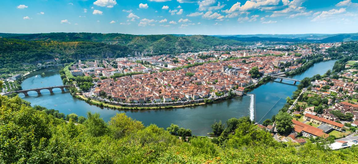 Aerial view of Cahors with the Lot River curving around the old town, framed by rolling green hills.