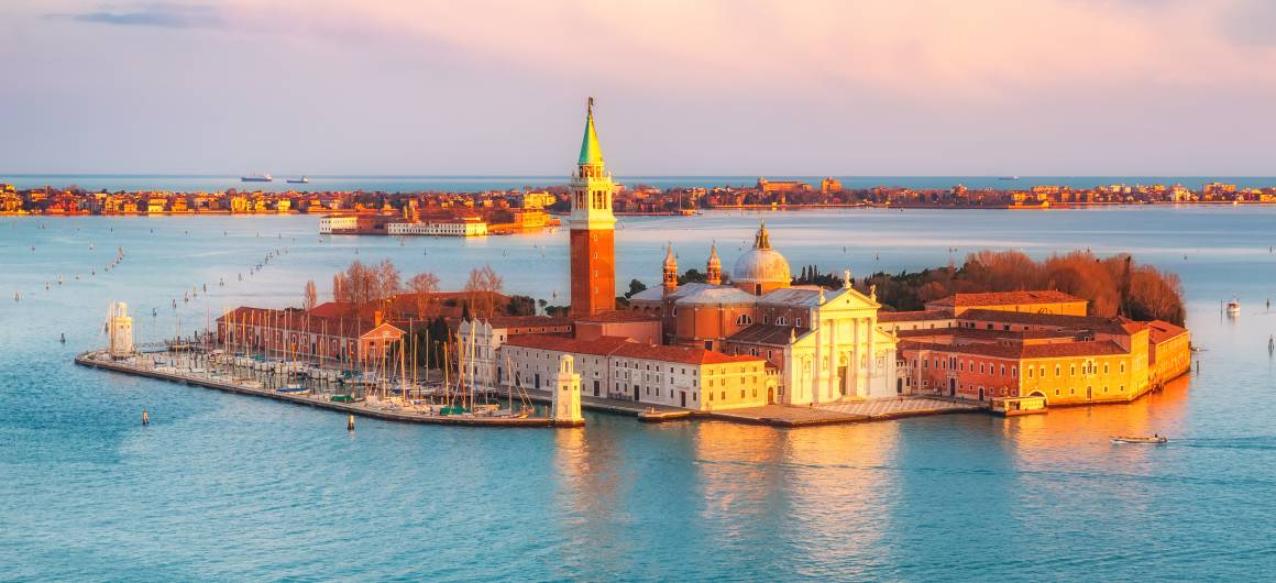 Island of San Giorgio Maggiore in the Venice Lagoon, seen at sunset with a boat gliding past.