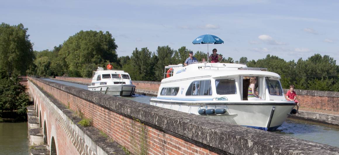 Un bateau traverse un pont de canal en briques sous le soleil d’Aquitaine.