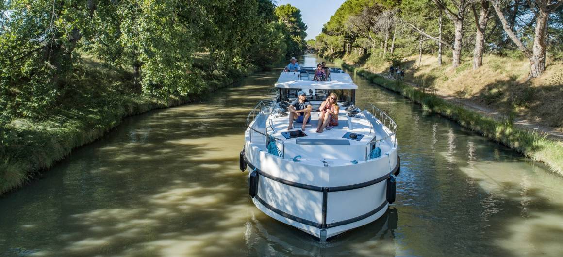 A canal boat sails through a tunnel of green, tree-lined waterways on the tranquil Canal du Midi in southern France.