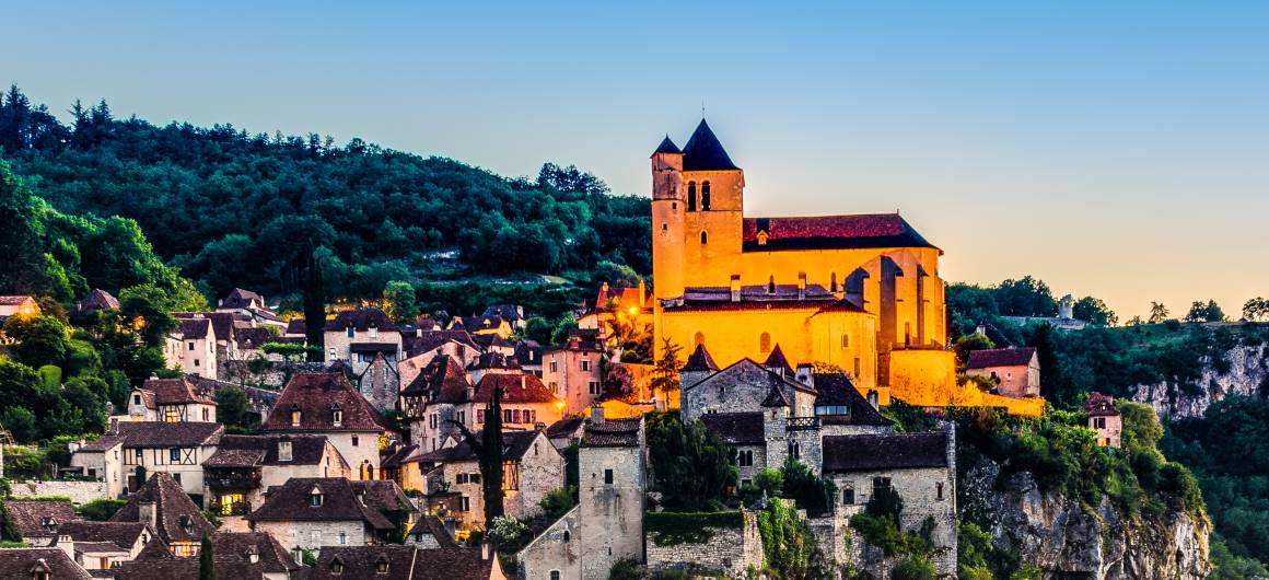 Sunrise over Saint-Cirq-Lapopie with the village glowing on the cliff’s edge and the Lot River curving below.