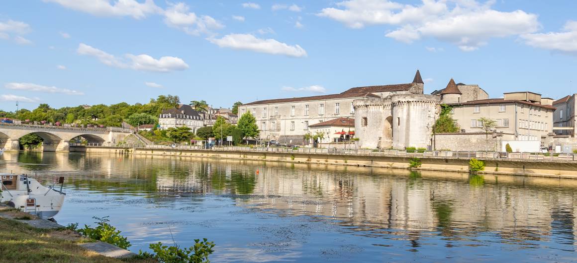 Stenen brug over de rivier de Charente in Cognac, met gebouwen van de oude stad die weerspiegelen in het kalme water op een zonnige middag.
