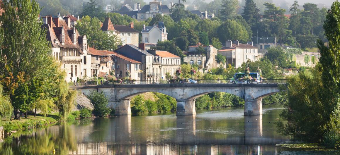 Charmante ville avec bâtiments historiques et pont reflétés dans la rivière.