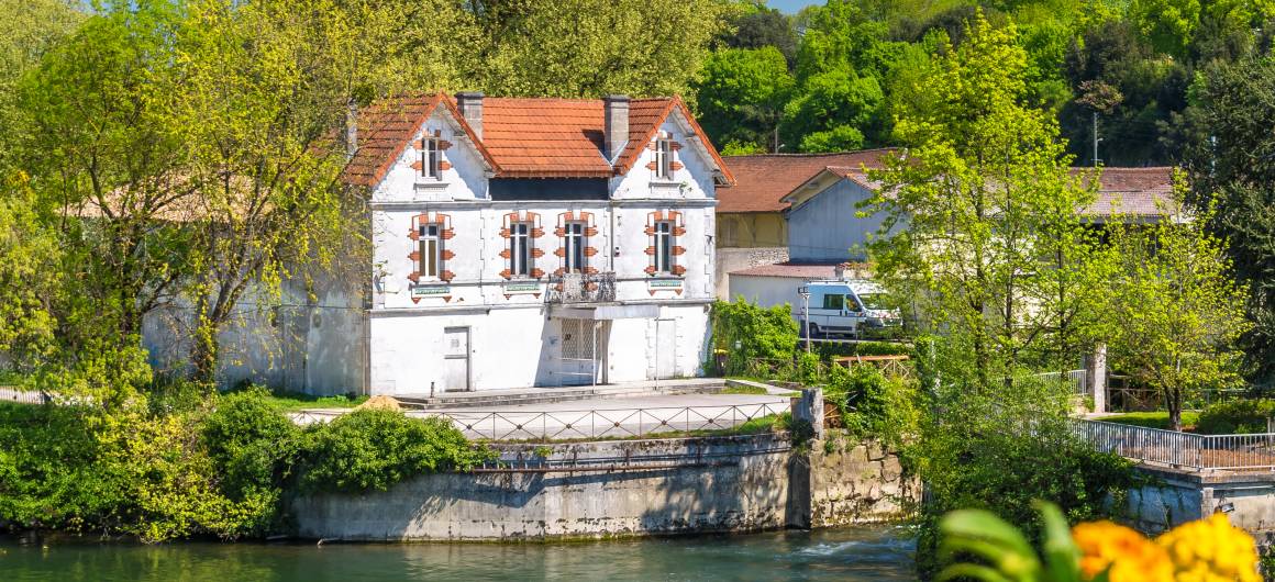Charmant huis aan de rivier in de Charente, omringd door bloeiende bloemen en weelderig groen onder een stralend blauwe hemel.