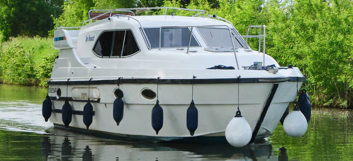 The Countess cruising slowly along a narrow, tree-lined waterway, its bow gliding smoothly through calm green reflections.