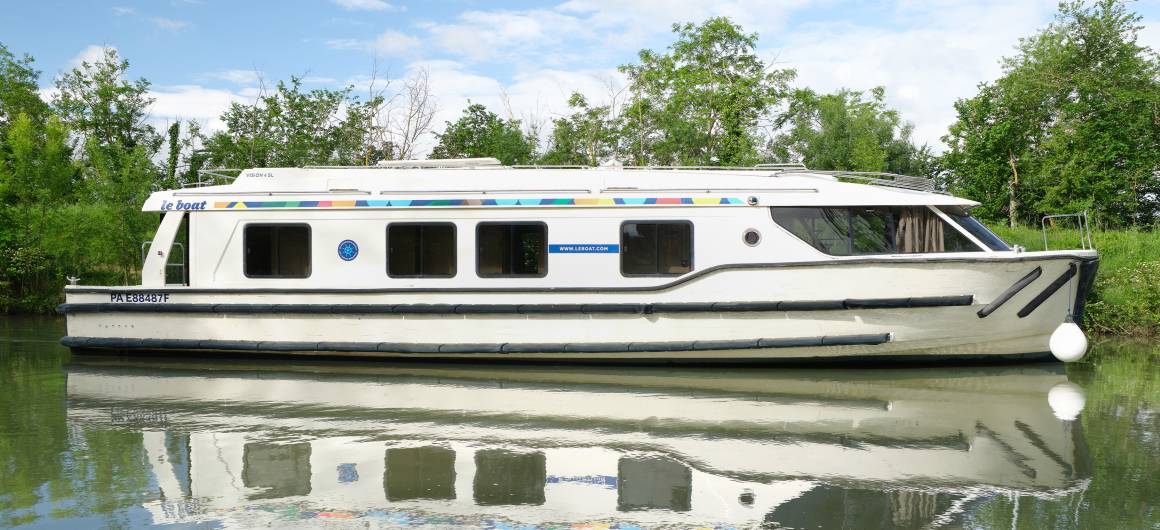 Vision 4 cruising along a scenic canal, reflected beautifully in the calm water.
