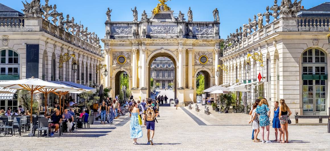 People strolling and enjoying cafés in the elegant Place Stanislas, framed by golden gates and classical architecture.