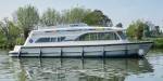 The Dancer 2 glides smoothly past overhanging trees on a tranquil stretch of river, its streamlined design and shaded windows reflected on the water.