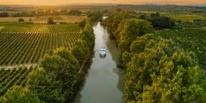 Una barca naviga verso il tramonto dorato sul Canal du Midi, attraversando vigneti e campagna rurale per un momento da cartolina in una vacanza fluviale francese.